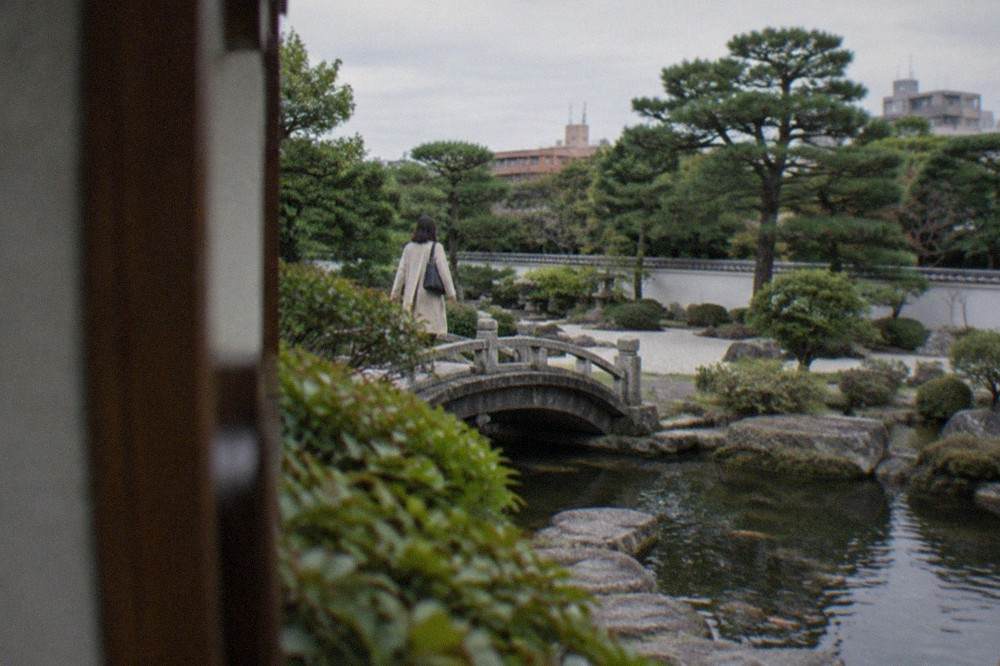 A stone path crossing a small arched bridge over a garden pond