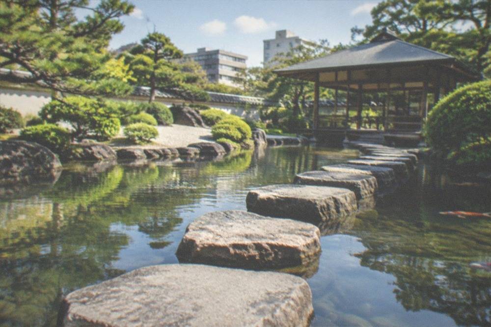 Stepping stones crossing a calm pond with a teahouse pavilion in the background