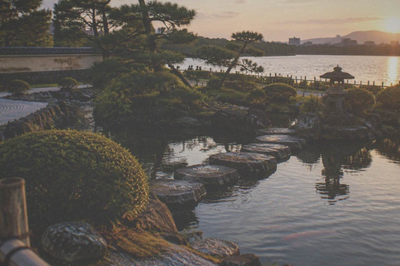 A traditional Japanese garden pond with stone lanterns and pine trees beside a large lake