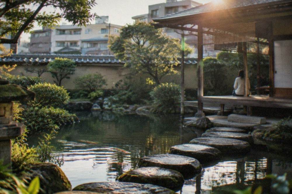 Stepping stones crossing a garden pond toward a wooden teahouse veranda