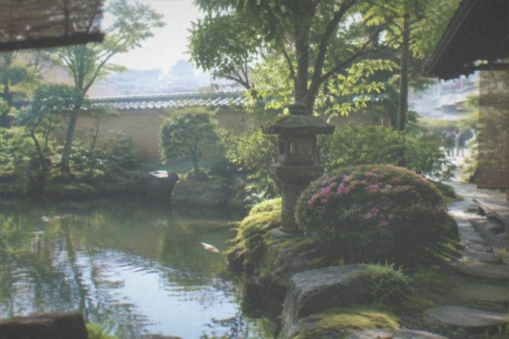 A stone lantern and clipped azalea beside a still pond reflecting trees