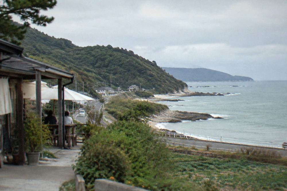 A quiet coast road curving along green hills above the sea on the Itoshima peninsula