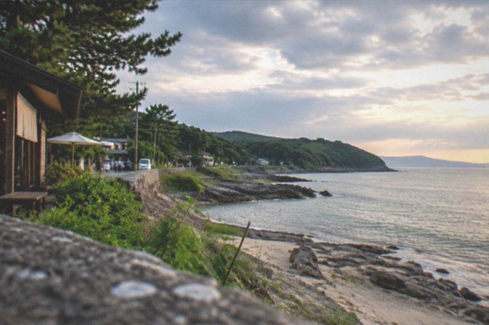 A wide view along the Itoshima coast with green headland, calm sea and a pale evening sky