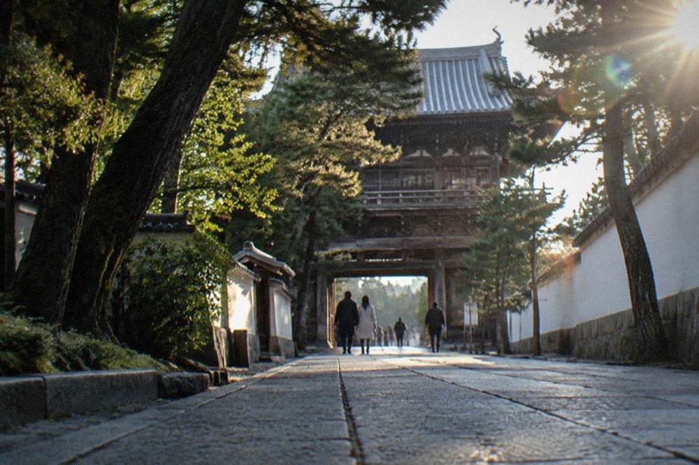 A tall wooden two-storey temple gate seen through trees