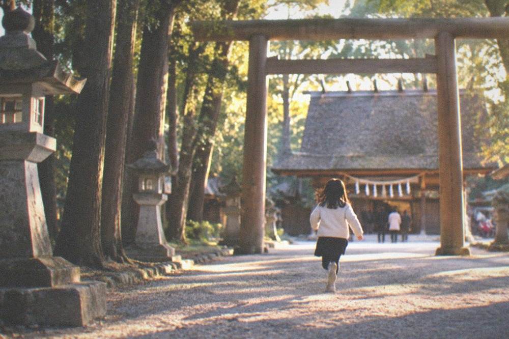 Gravel courtyard in front of a wooden shrine hall with a rope and paper streamers