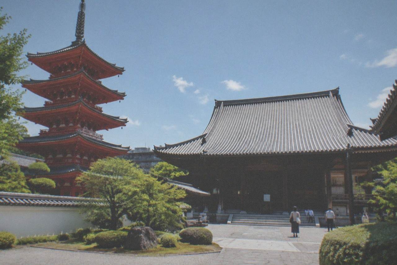 A large wooden temple hall with a wide roof and stone paving under a clear sky
