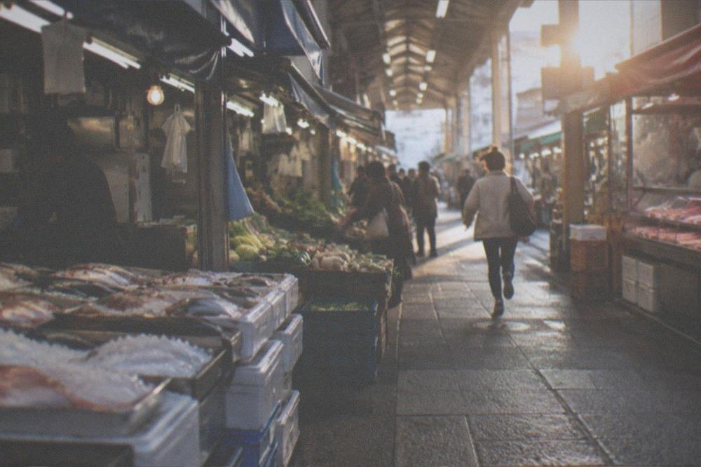 Morning shoppers browsing vegetable and pickle stalls under the arcade roof