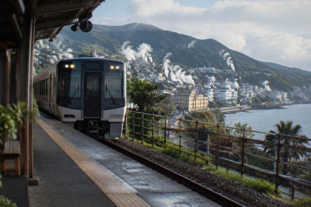 A limited express train standing at a station platform beside coastal hills