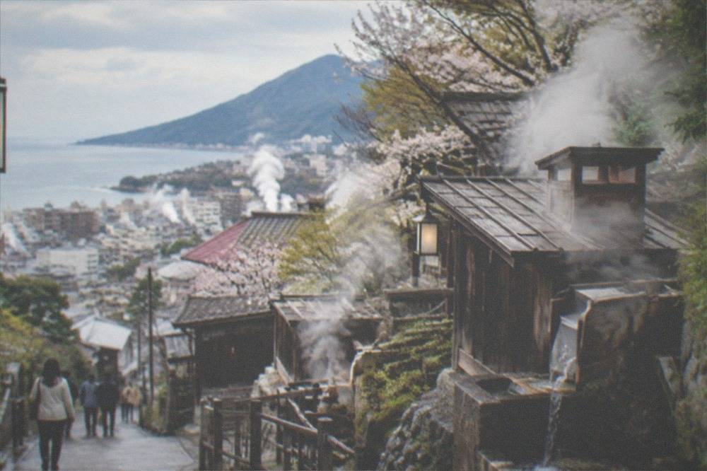 Wooden huts on a hillside releasing steam from hot spring water channels