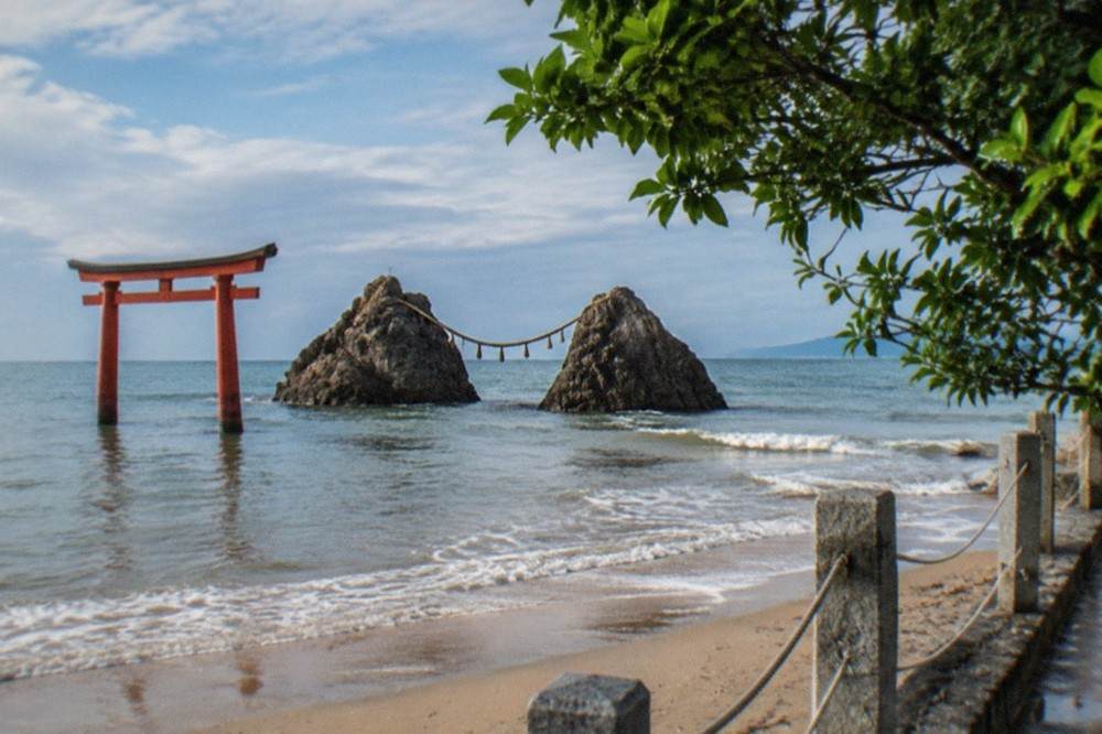 Twin rocks standing in shallow water beside a sandy beach with a torii gate