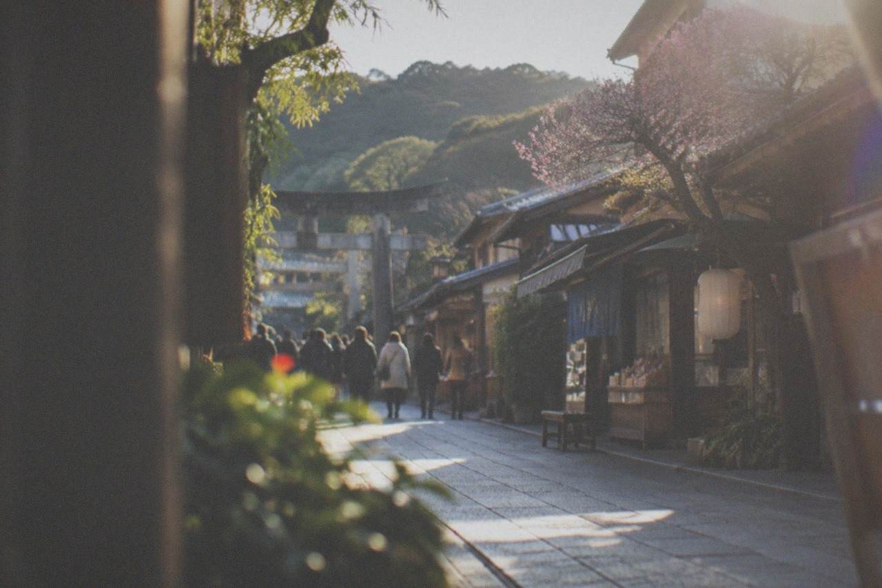 A shrine approach street lined with traditional shopfronts leading toward a torii gate