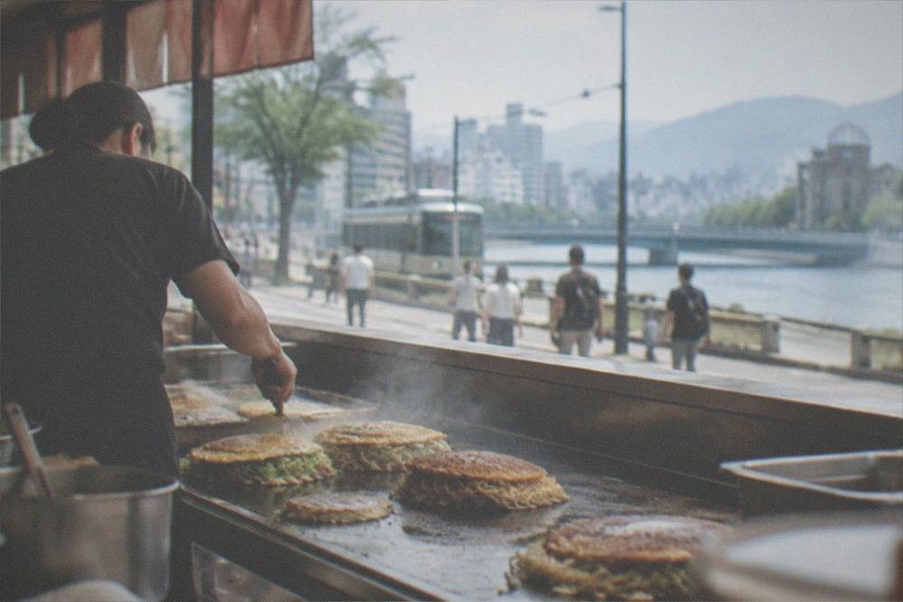 A cook preparing layered savoury pancakes on a flat griddle counter