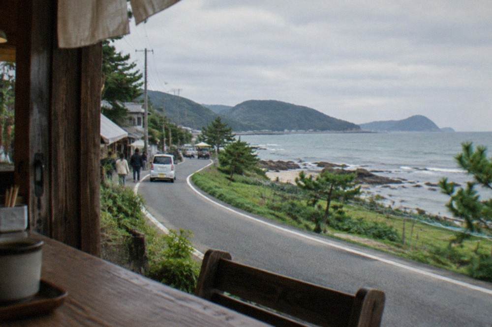 Narrow coast road curving past green hills with the sea beyond