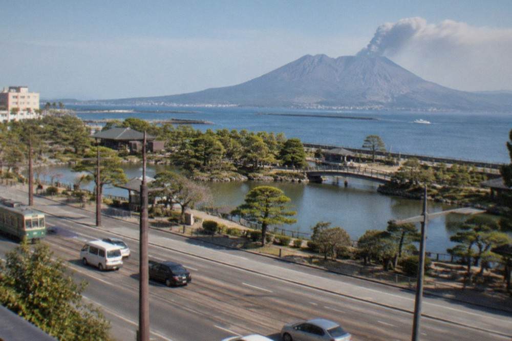 A traditional Japanese garden pond with a volcano rising across a bay in the background