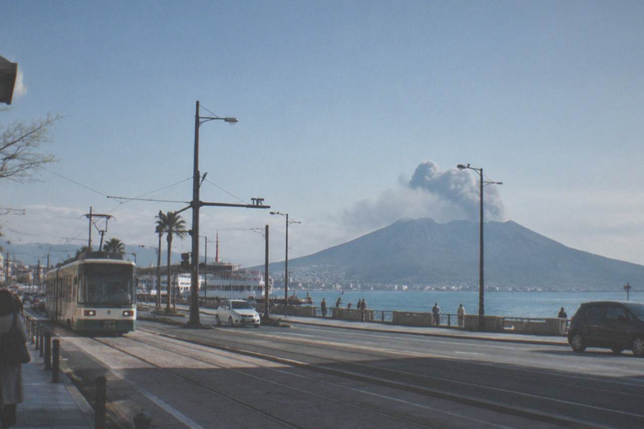 A Shinkansen train at a station platform under a bright sky with mountains in the distance