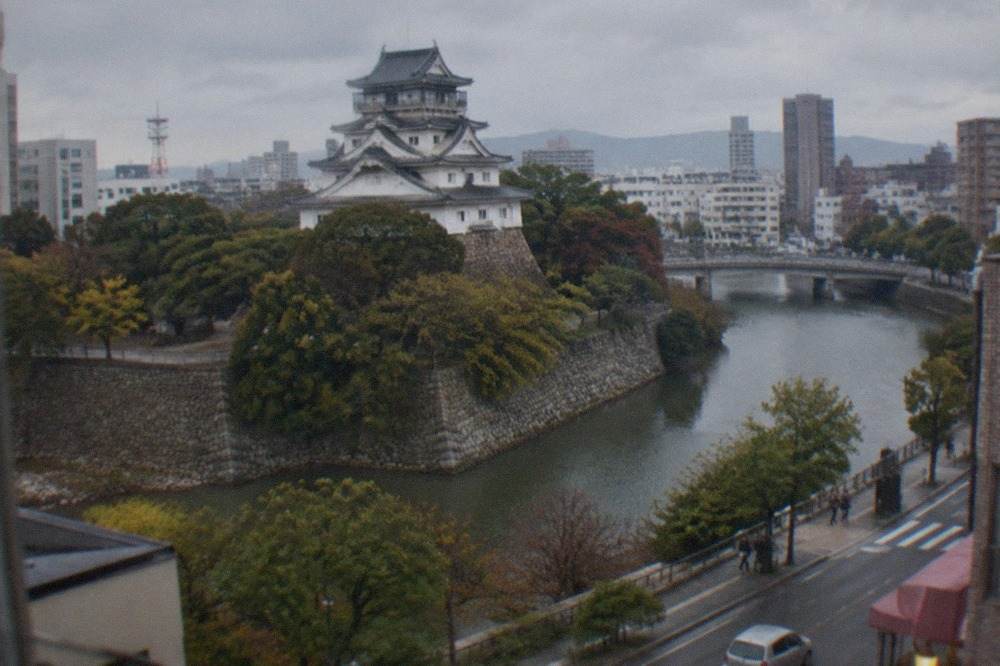 Kokura Castle keep rising above trees with the modern city skyline behind it
