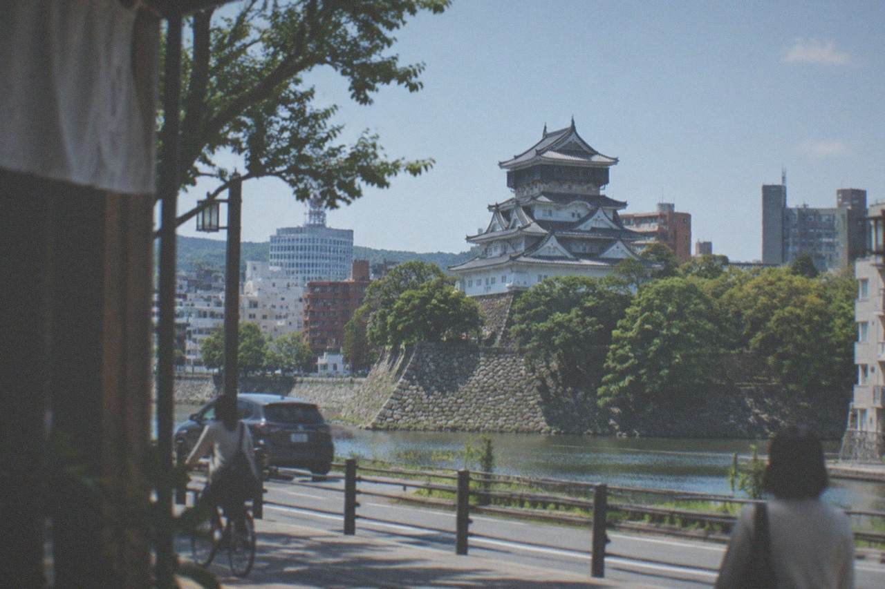 Kokura Castle keep rising above trees with the modern city skyline behind it
