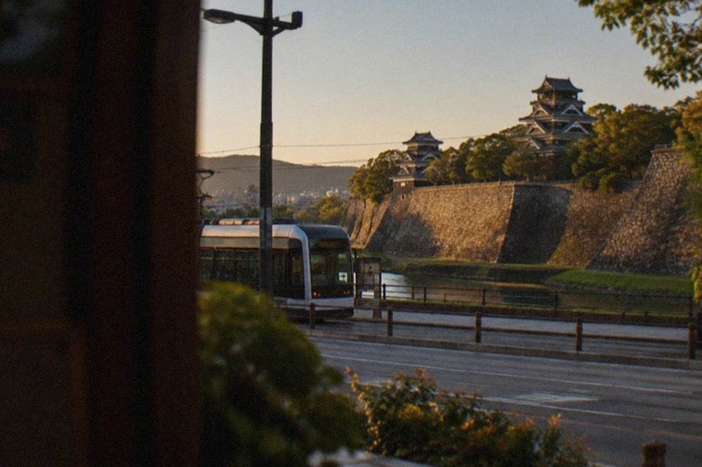 Kumamoto Castle stone walls and keep rising above tree-lined moats under a clear sky