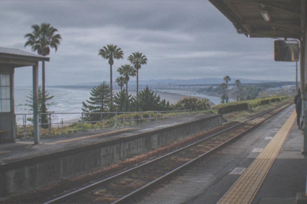 A quiet Japanese train station platform in the early morning with sunlight across the tracks
