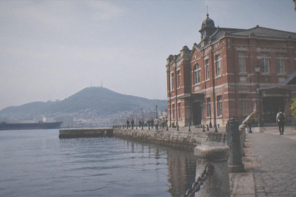 A red brick customs building beside a calm harbour with hills visible across the water