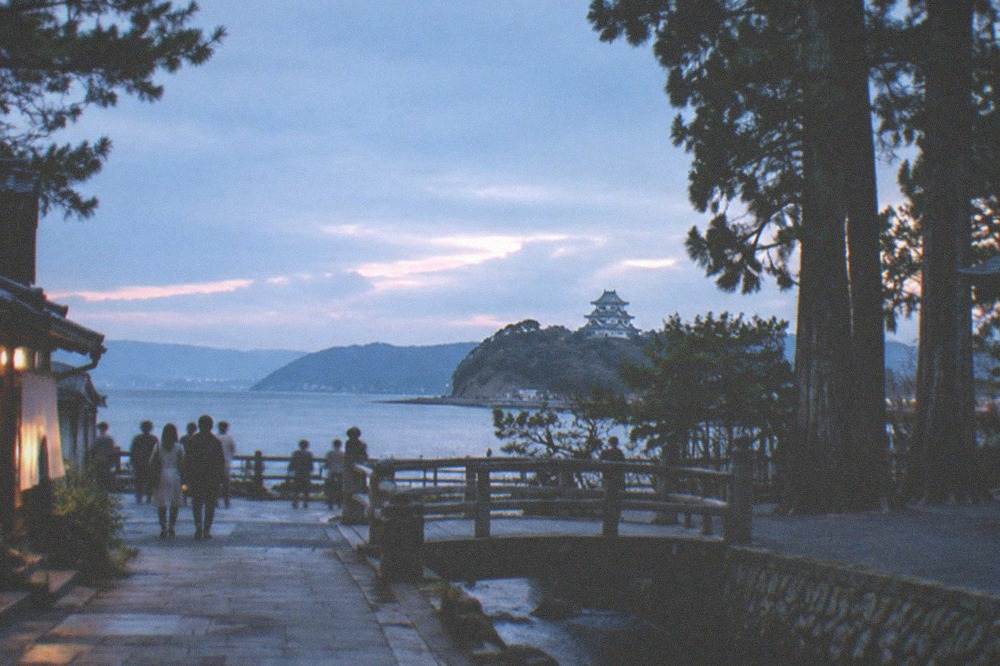 A coastal castle keep seen across water with distant hills behind