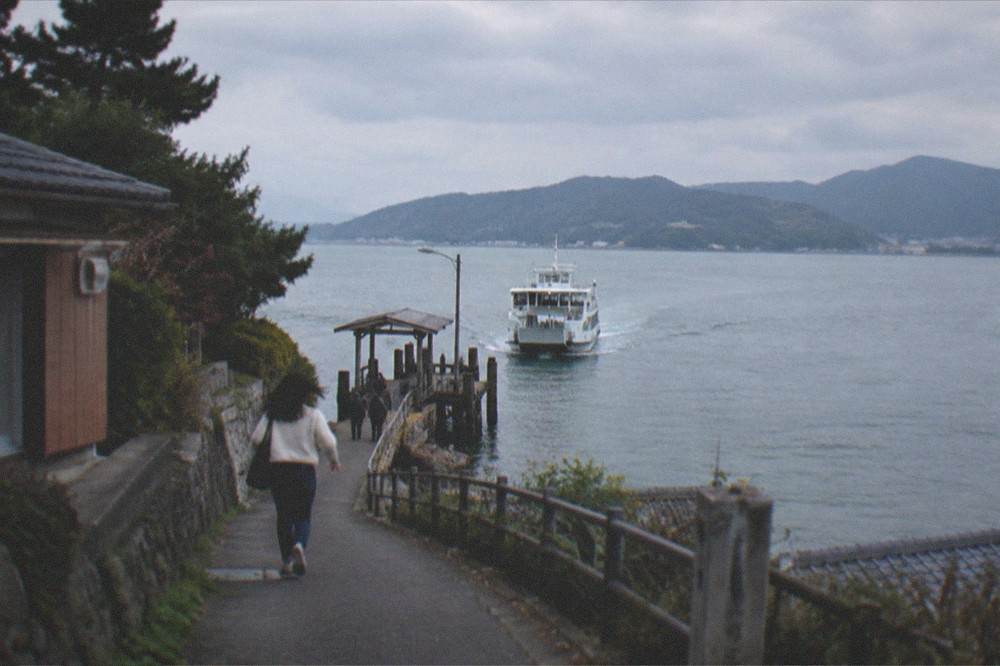 Ferry approaching a wooden island jetty in late afternoon light with hills behind