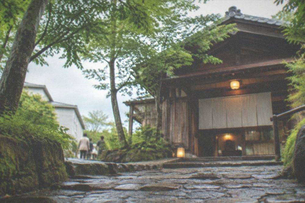 A stone path leading through trees toward a traditional wooden bathhouse entrance