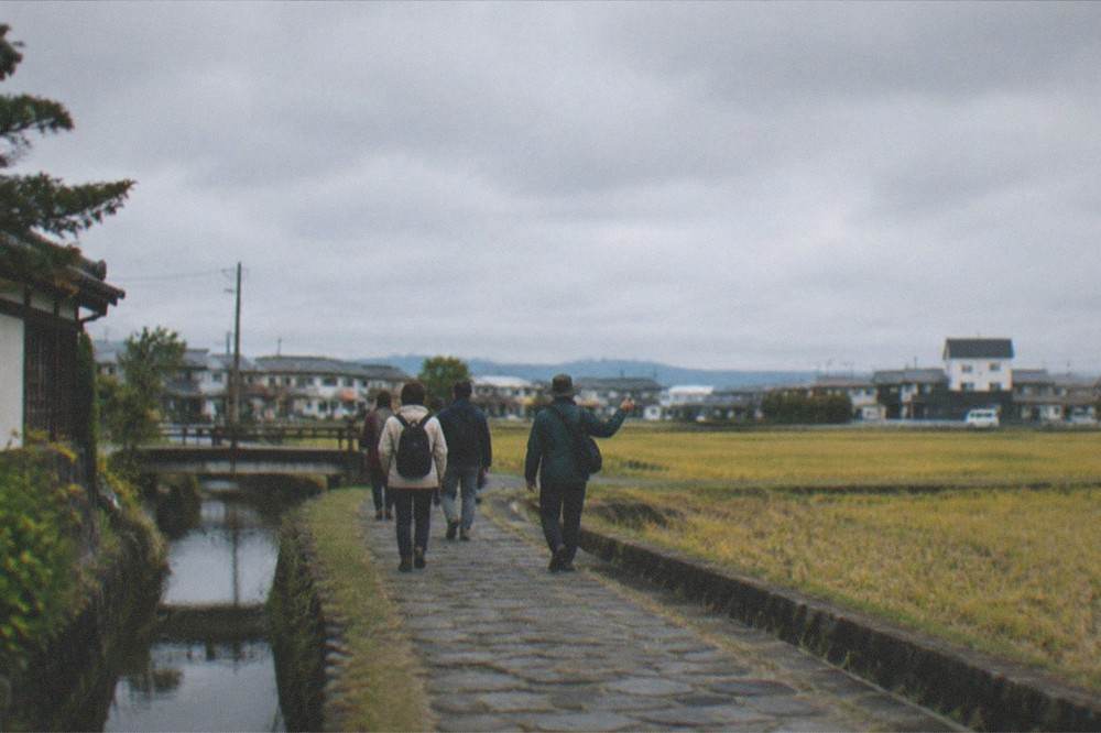 A small group of travellers walking with a guide along a rural stone path in Kyushu