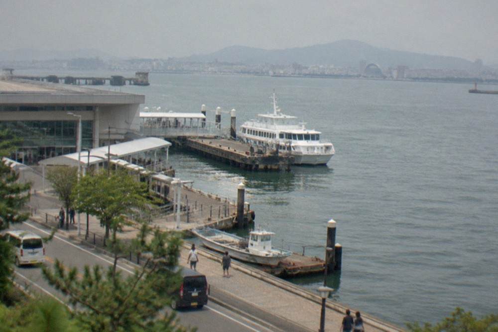 A ferry terminal jetty in Hakata Bay with a white passenger boat tied up at the pontoon