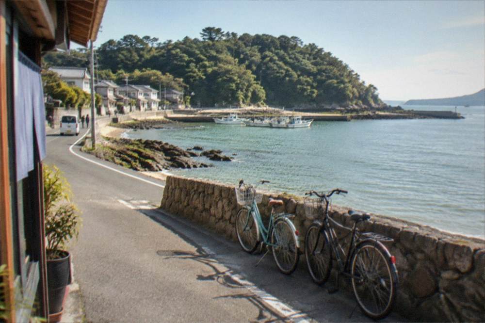 A couple of bicycles leaning against a low stone wall beside a coastal road on a small island