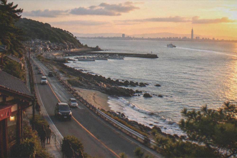 A ferry wake spreading across calm bay water with a city skyline in the far distance at late afternoon