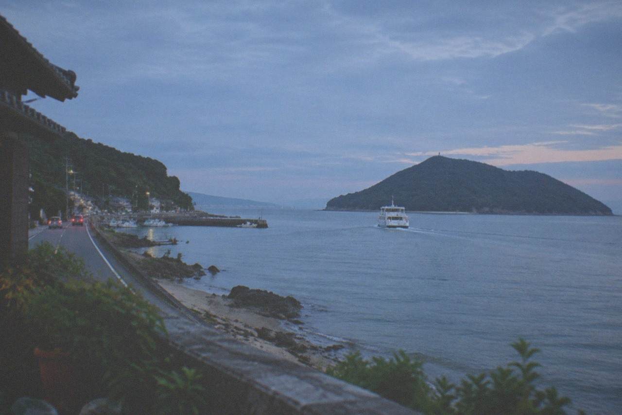 A small passenger ferry crossing calm blue water toward a green island under a bright sky