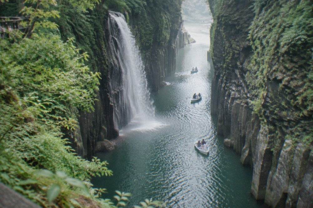 Steep volcanic cliffs enclosing a narrow river gorge with a waterfall dropping toward calm green water