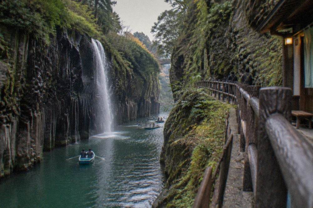 A narrow pedestrian walkway clinging to the cliff edge above a green river running through a gorge