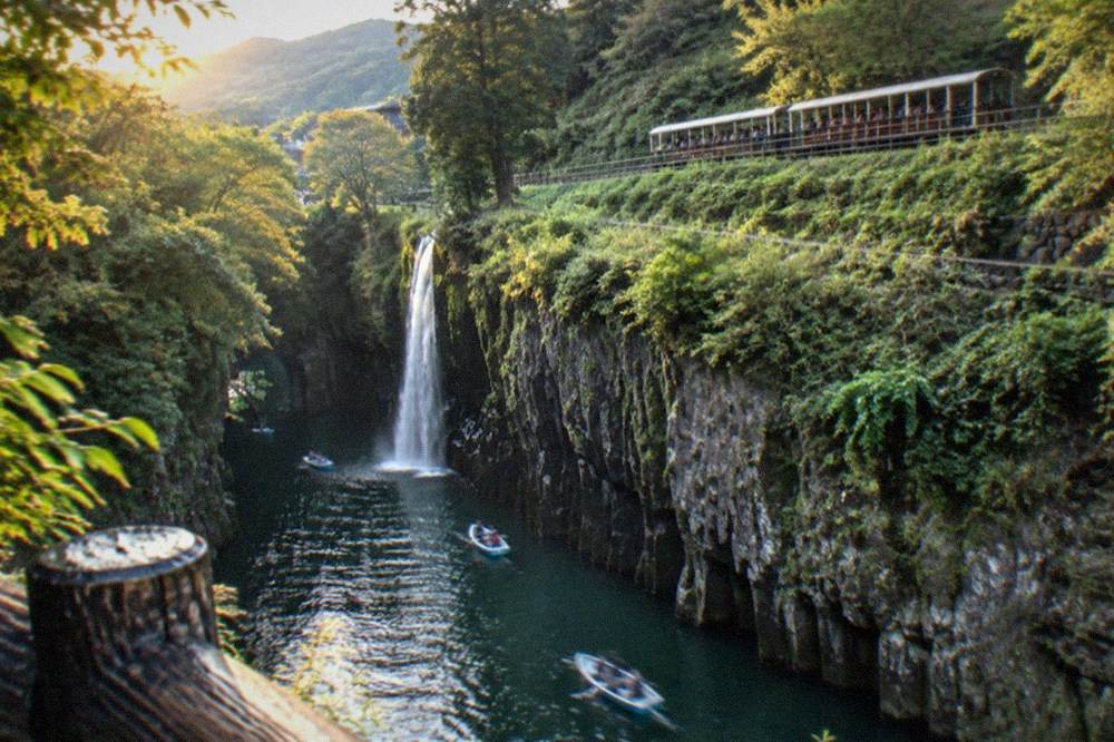 An open-sided sightseeing train travelling along a green hillside track above a river valley