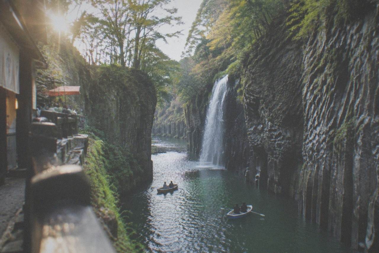 Steep volcanic cliffs enclosing a narrow river gorge with a waterfall dropping toward calm green water