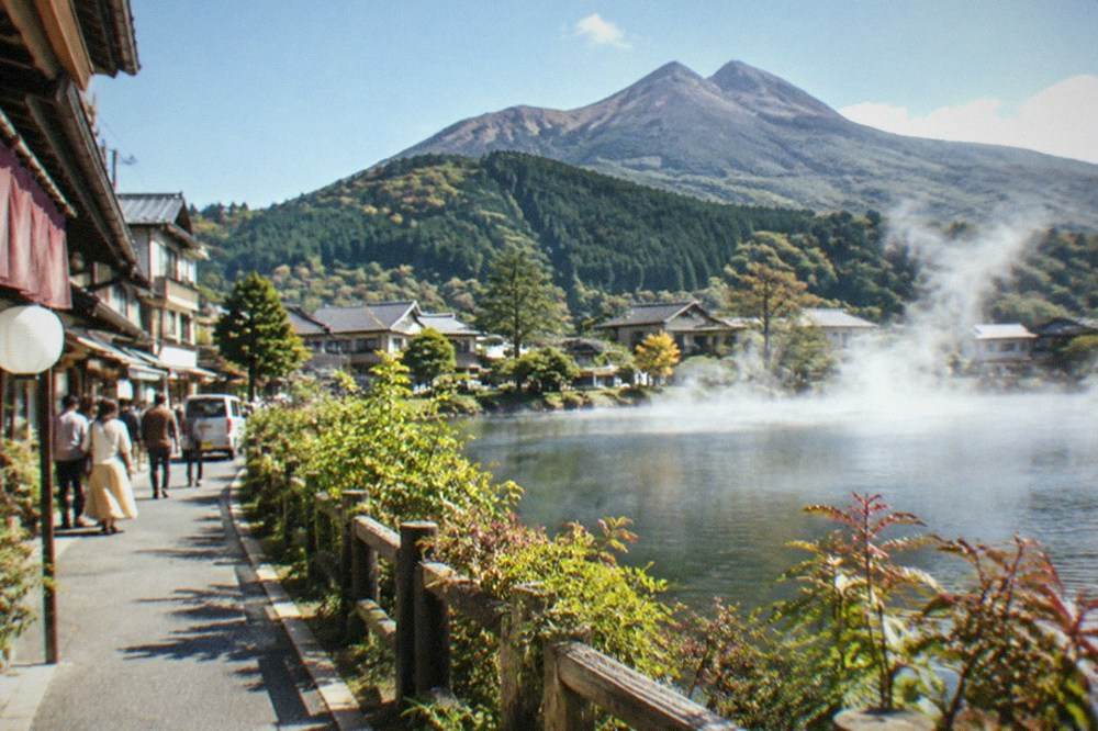 Steam rising from a lake at the edge of a small town with forested hills beyond