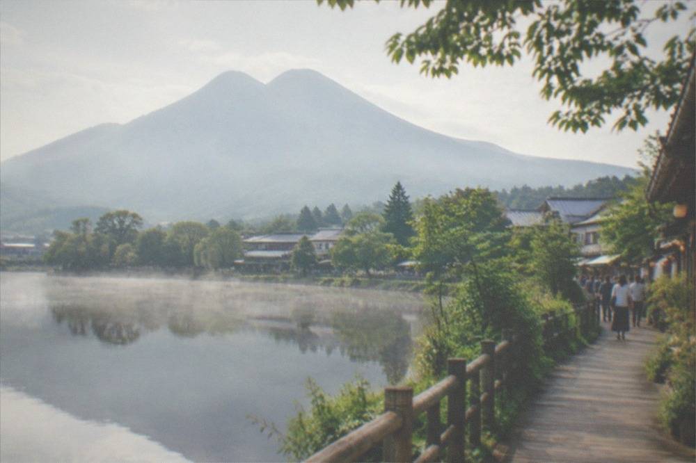 A wooden boardwalk path beside a misty lake with trees reflected in the water