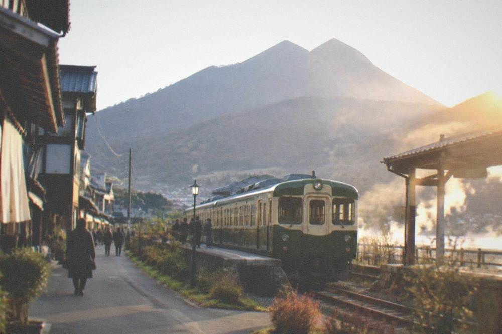 A green and cream sightseeing train waiting at a small rural station platform