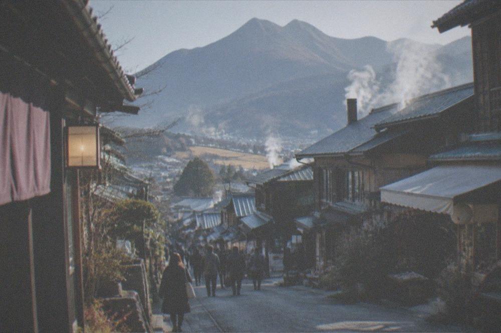 A quiet street of low wooden buildings with steam drifting over rooftops in a mountain valley