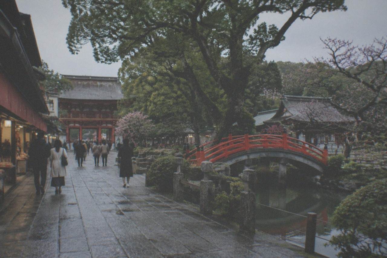 Stone approach path lined with shops leading toward a vermilion shrine gate among trees