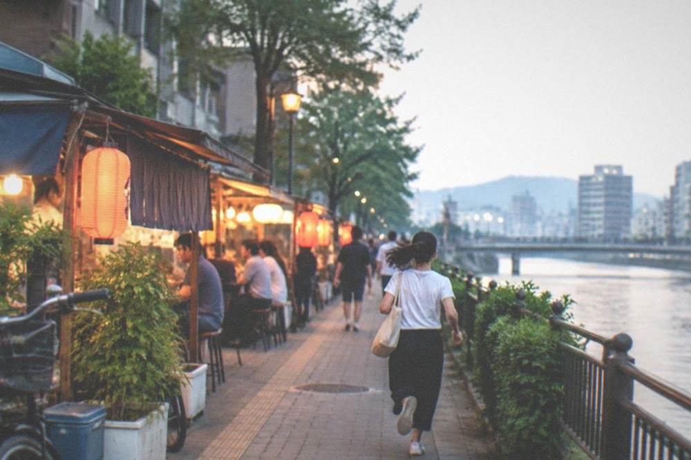 Row of small lit street food stalls along a riverside street at night