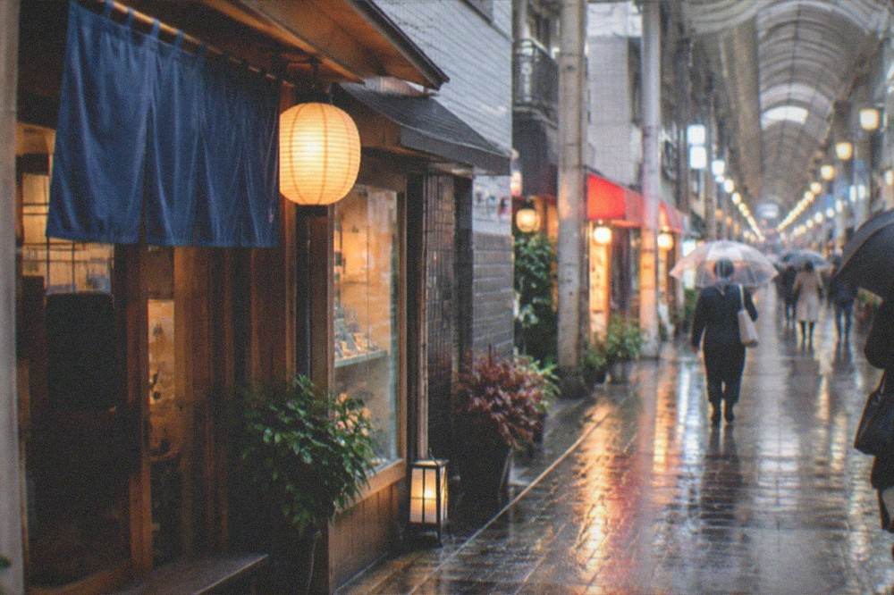A rainy day view of a covered street in Hakata with illuminated shopfronts