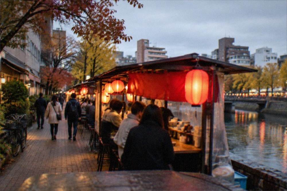 Red lanterns glowing above a row of street food stalls along a river at night