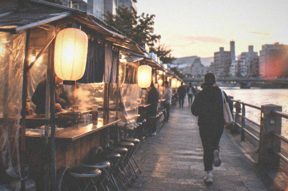 A row of glowing yatai food stalls lined along a river at night