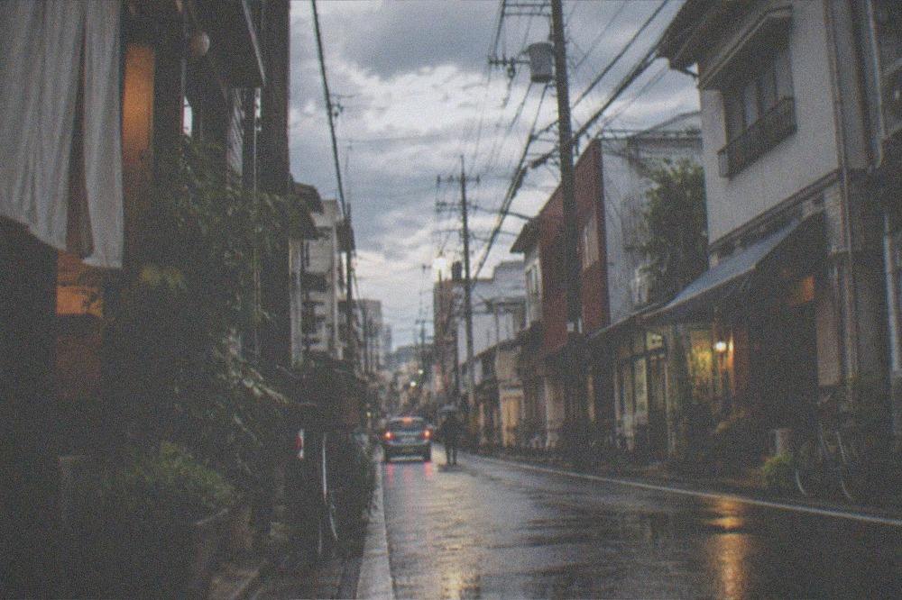 A rain-slicked city street at night with bar signs reflected in puddles