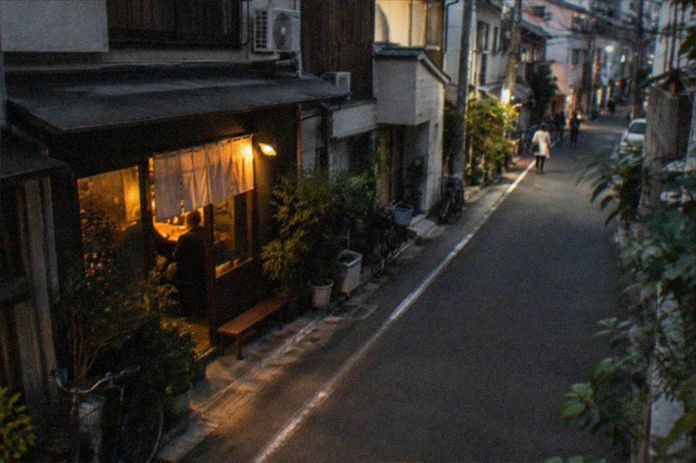 A late-night street corner with a small bar's light spilling onto the pavement