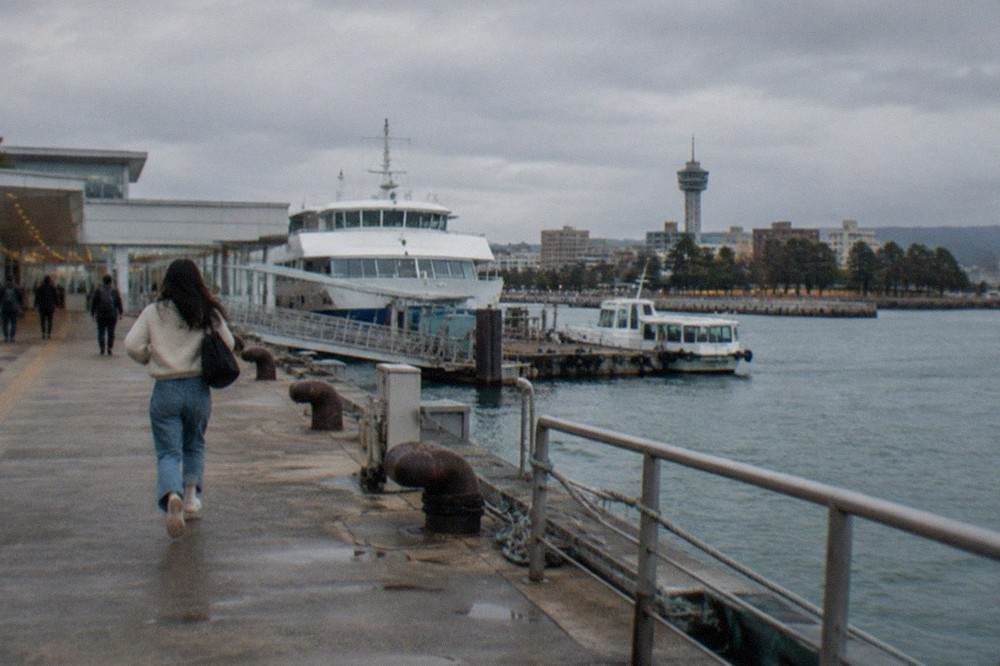 A boat deck at dusk with a modern observation tower and illuminated waterfront buildings in the distance