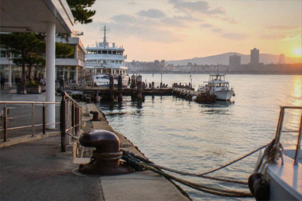 A small boat moored at a wooden pier with a city skyline across the water behind it