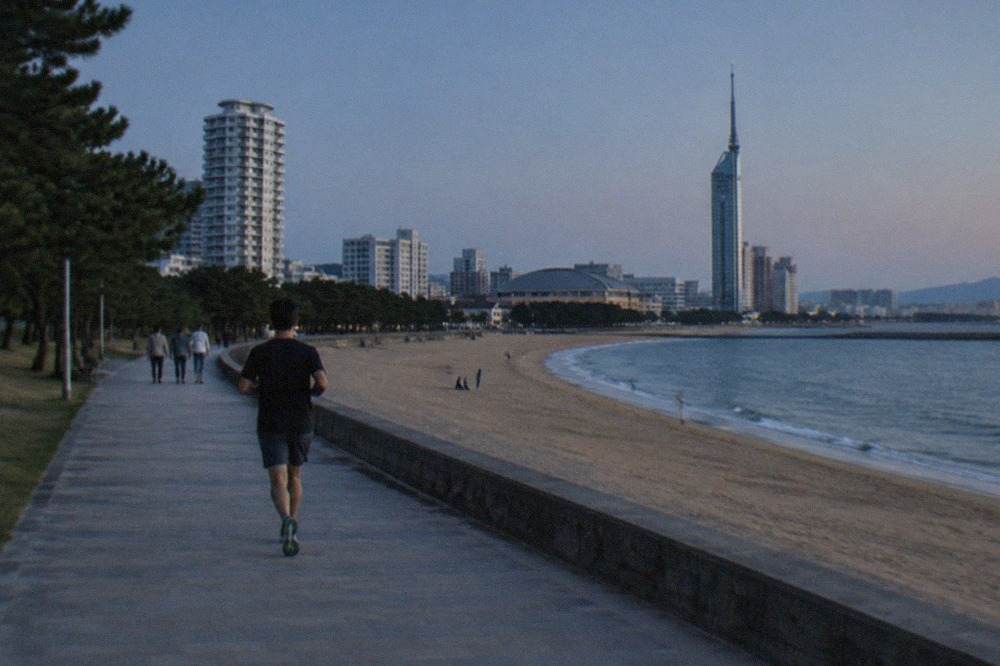 A wide sandy beach curving along a calm bay with a tall seaside tower in the background under a clear sky